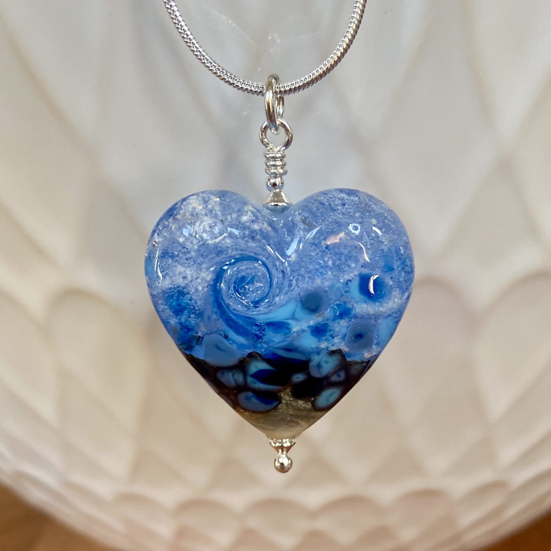 A flame worked blue glass heart-shaped pendant with cremated ashes